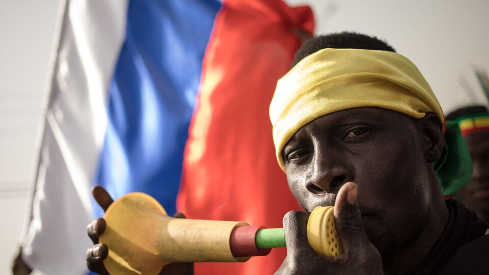 Un manifestant souffle dans une vuvuzela tandis qu'un autre brandit un drapeau russe lors d'une manifestation organisée pour célébrer l'annonce de la France de retirer les troupes françaises du Mali.