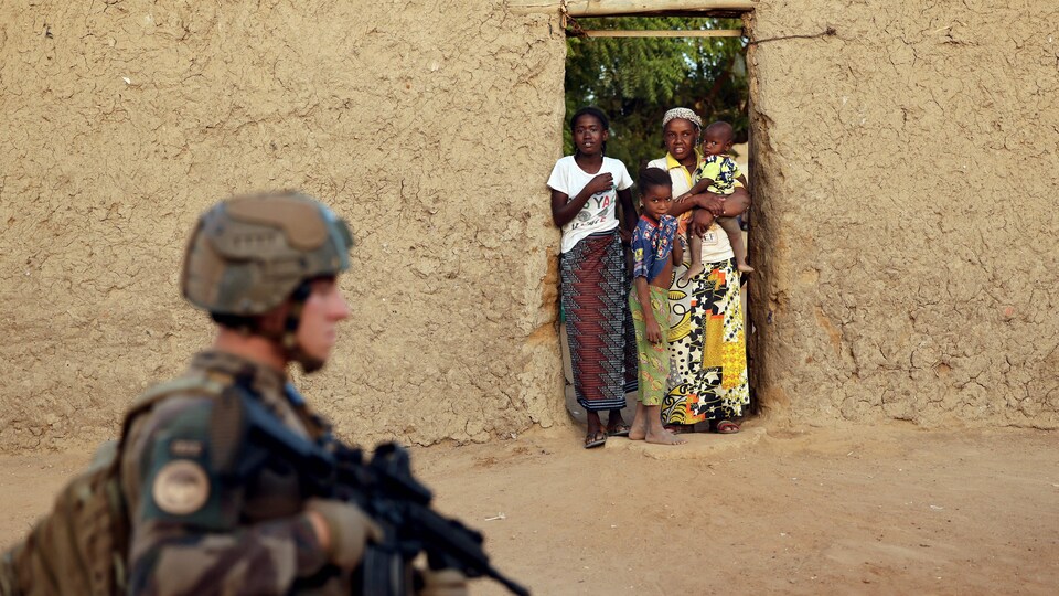 Un soldat passe devant l'entrée d'une maison où se trouve une famille.