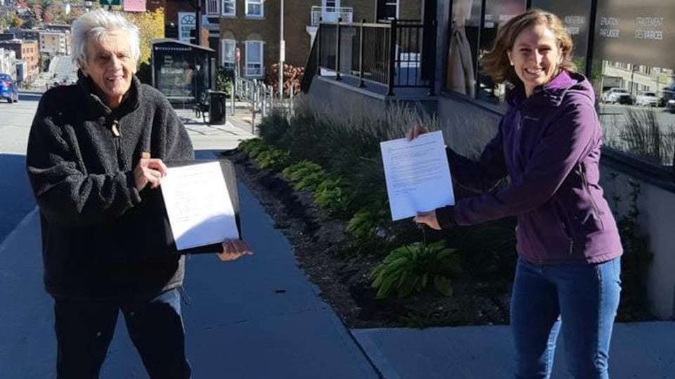 Jacques Malouin et Christine Labrie tiennent chacun une copie de la pétition en se tenant à distance l'un de l'autre.