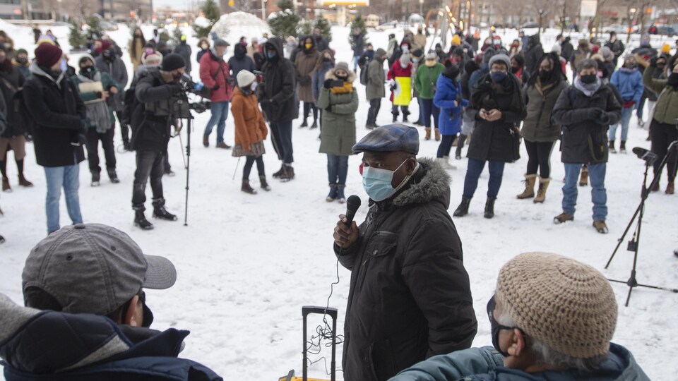 Un homme tient un micro face à une foule statique respectant les règles de distanciation.