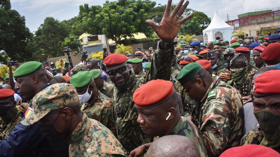 Mamady Doumbouya, entouré de nombreux militaires au milieu d'une foule, fait un salut de la main gauche.