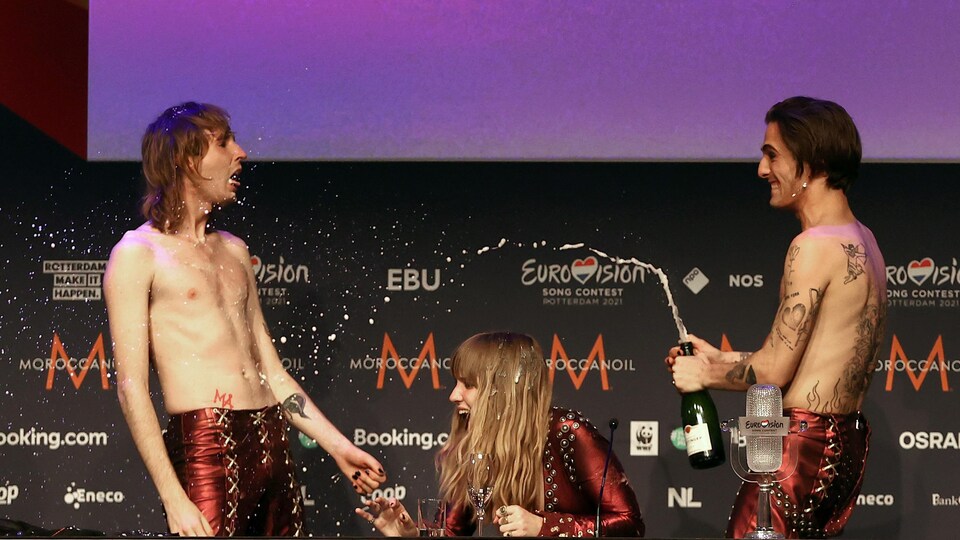 Deux hommes et une femme sur scène en train de s'asperger de champagne. 