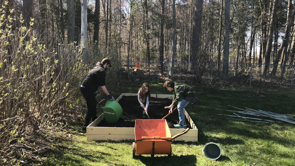 Un homme et deux enfants jouent dans la terre d'un jardin.