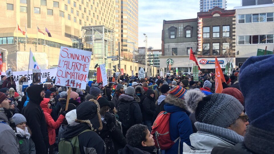 Plusieurs personnes se tiennent debout au centre-ville de Montréal, certaines brandissant des pancartes ou des drapeaux.