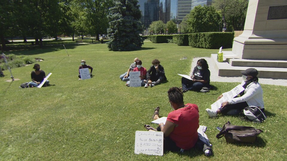 un groupe de personnes assises dans l'herbe, avec des pancartes Black Lives Matter