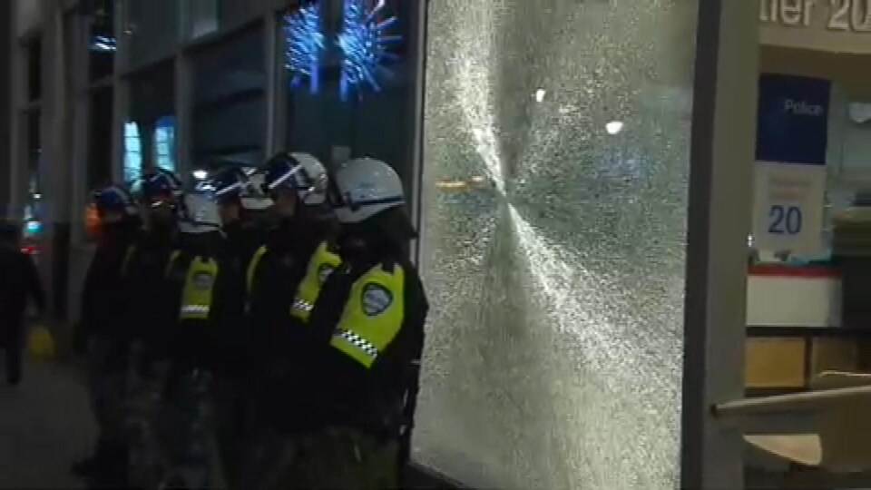 Des policiers devant la vitrine fracassée du poste de quartier 20 à Montréal