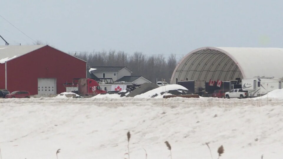 Des camions et véhicules stationnés près d'une ferme, dehors, en hiver.