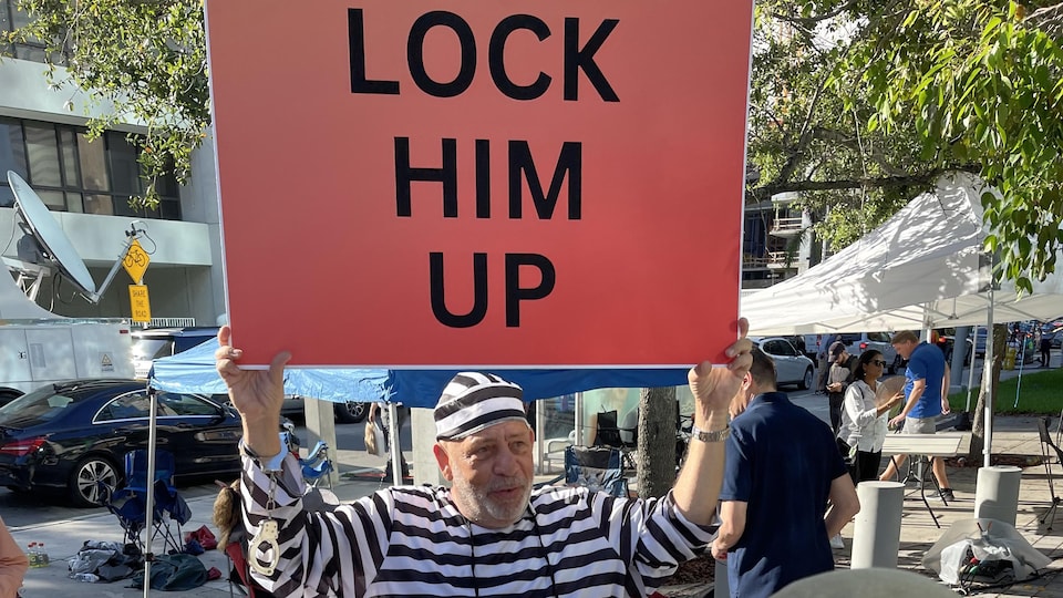 A man dressed as a prisoner holds a sign calling for Donald Trump to be jailed.