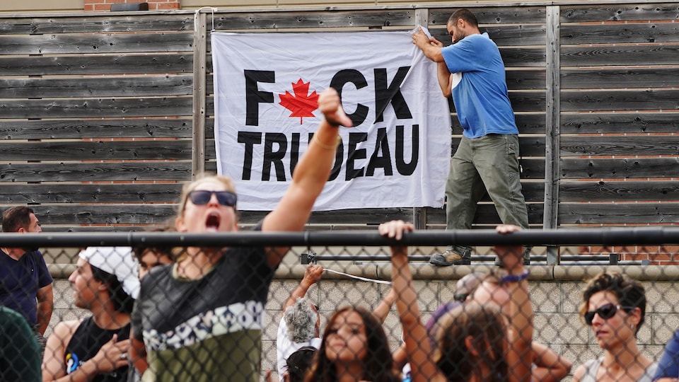 People are screaming from behind the fence.  An opponent hung a sheet of paper insulting Justin Trudeau.