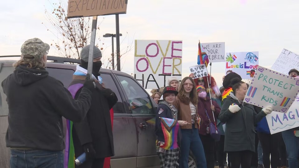 Un groupe de manifestants brandissent des pancartes qui affichent des messages de soutien à la communauté LGBTQ de Calgary.