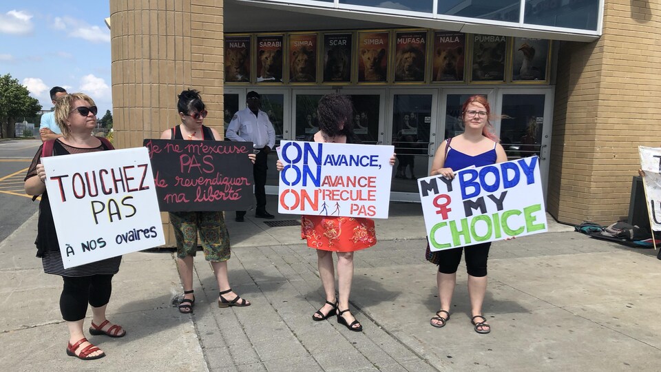 Quatre manifestantes portent des pancartes devant le cinéma. On peut notamment y lire « Touchez pas à nos ovaires ».