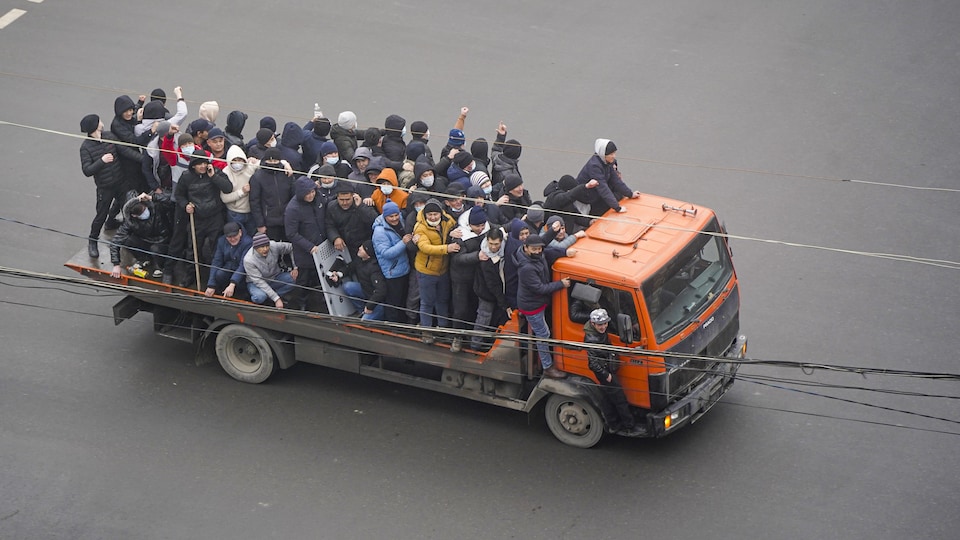 Des dizaines d'hommes s'entassent sur la plate-forme d'un camion.