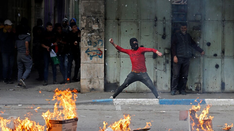 Un homme masqué lançant une pierre avec des hommes derrière lui. 