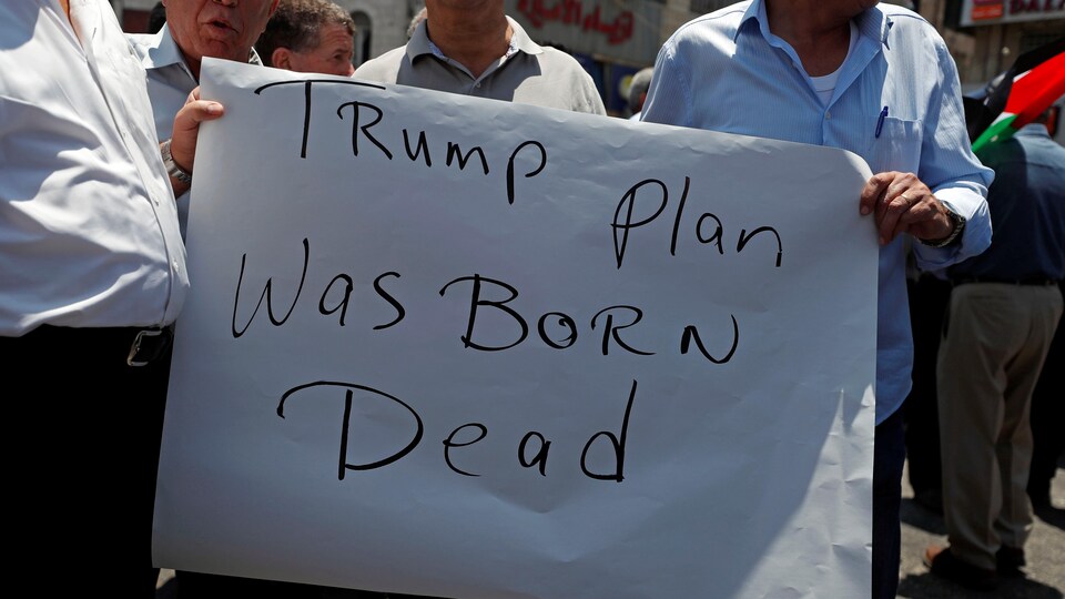 Des hommes tiennent une affiche où il est écrit en anglais: le plan de Trump est mort-né.