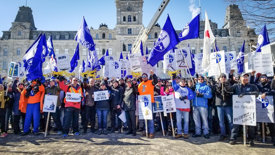 Des manifestants, pancartes en main et poing levé, se tiennent devant l'Assemblée nationale du Québec.