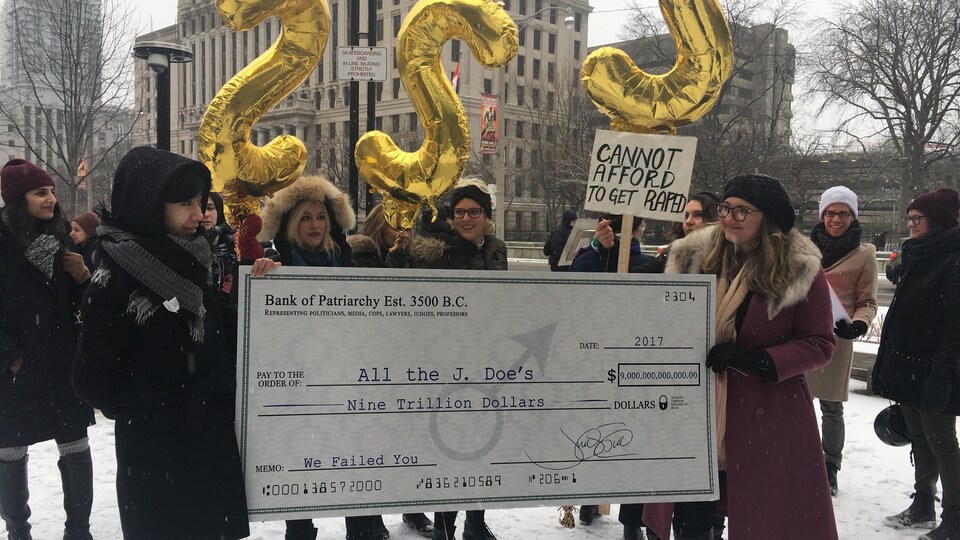 Des manifestantes tiennent un chèque géant pour réclamer des indemnités aux gouvernements.
