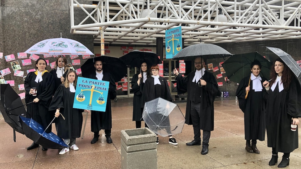 Des avocats manifestent devant le palais de justice avec des parapluies.