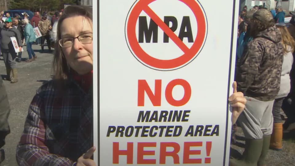 Une manifestante tient une pancarte sur laquelle est inscrit un message d'opposition à la création de toute aire marine protégée.