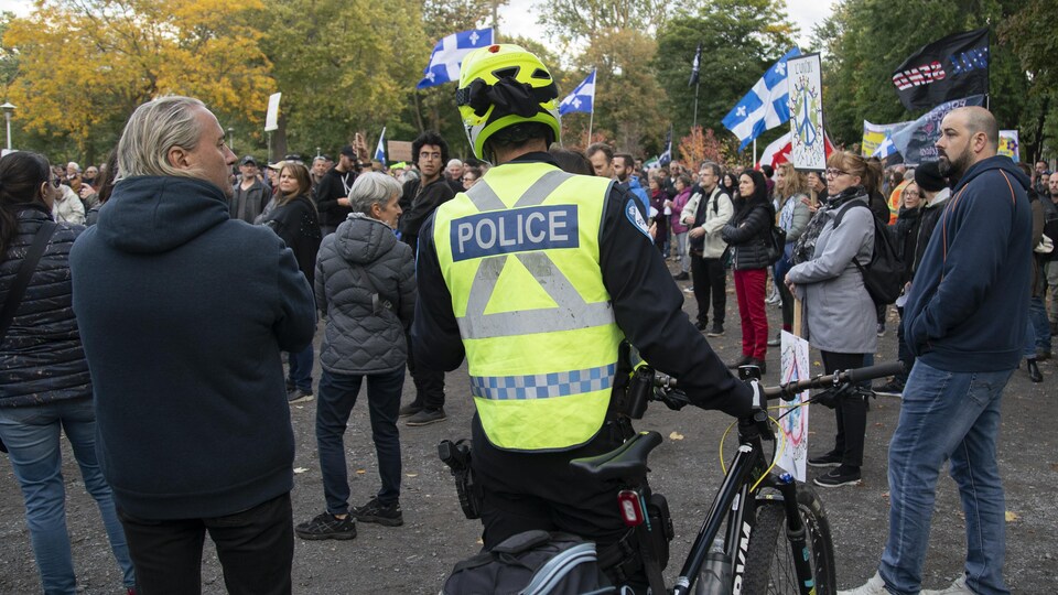 Un policier à vélo au milieu de manifestants qui protestent contre le port obligatoire du masque.
