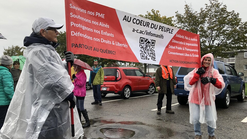 Deux personnes tiennent une bannière avec l'inscription « Au cœur du peuple ». La dame à droite sourit.