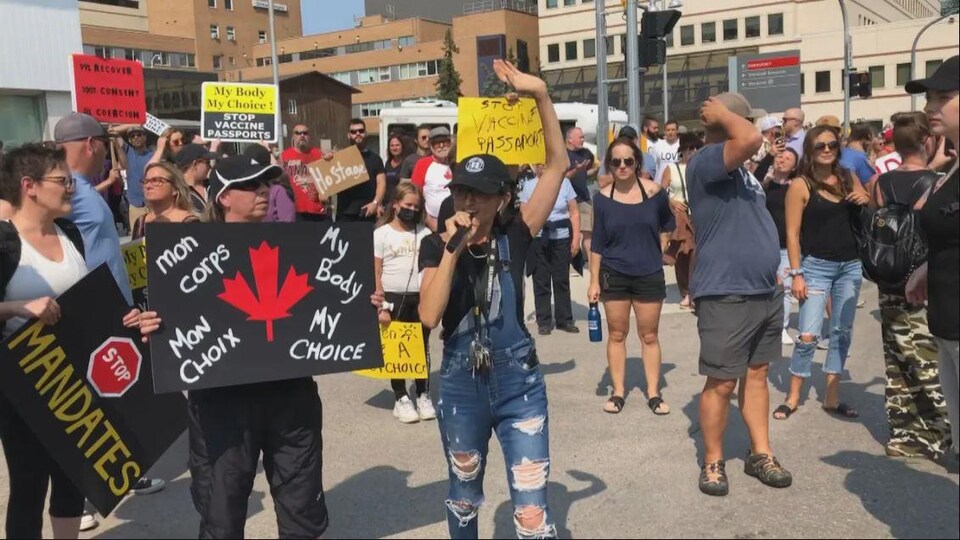 Des manifestants tiennent des affiches pour s'opposer à la vaccination et au passeport vaccinal devant devant le Centre des sciences de la santé de Winnipeg.