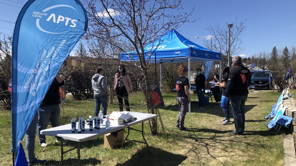 Des membres de l'APTS discutent autour d'une tente aux couleurs du syndicat.