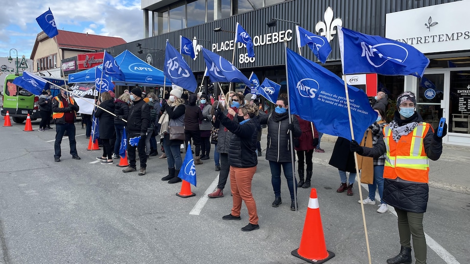 Des manifestants tenant des drapeaux de l'APTS devant la Place du Québec.