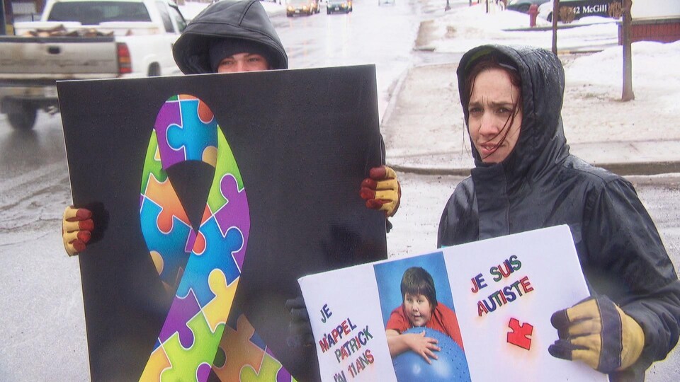 Deux personnes tiennent des pancartes dans la pluie.