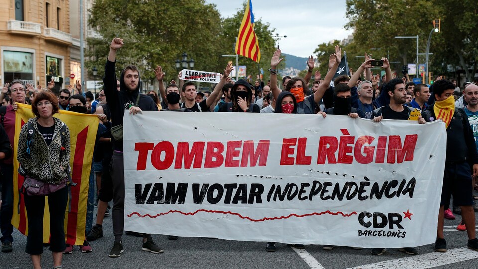Des manifestants catalans en faveur de l'indépendance manifestent dans les rues de Barcelone, tenant une banderole sur laquelle on peut lire : « Faisons tomber le régime ».