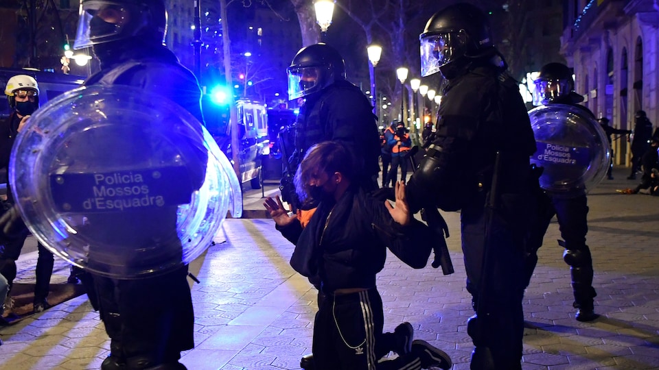 Des policiers encerclent un manifestant à genoux, les mains levées.