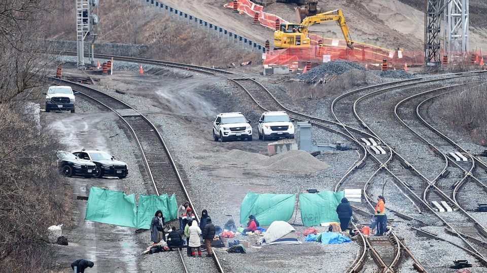 Une dizaine de personnes sont assises près de tentes installées sur les rails.