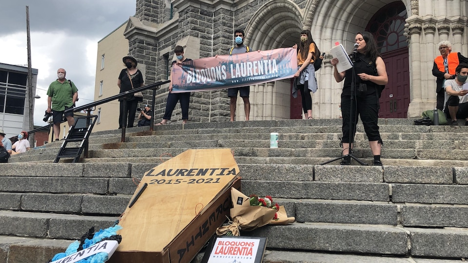 Les organisateurs de la manifestation s'adressent à la foule sur le parvis de l'église Saint-Roch, en avant-plan on voit un cercueil sur lequel on peut lire Laurentia.
