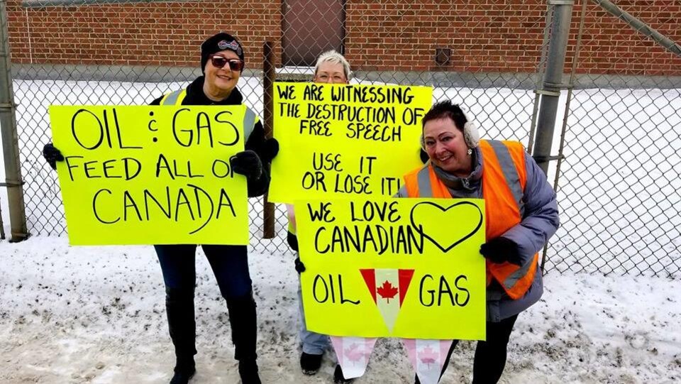 Trois manifestantes à Brandon debout sur la neige brandissent des pancartes qui appuient l'industrie pétrolière et gazière.