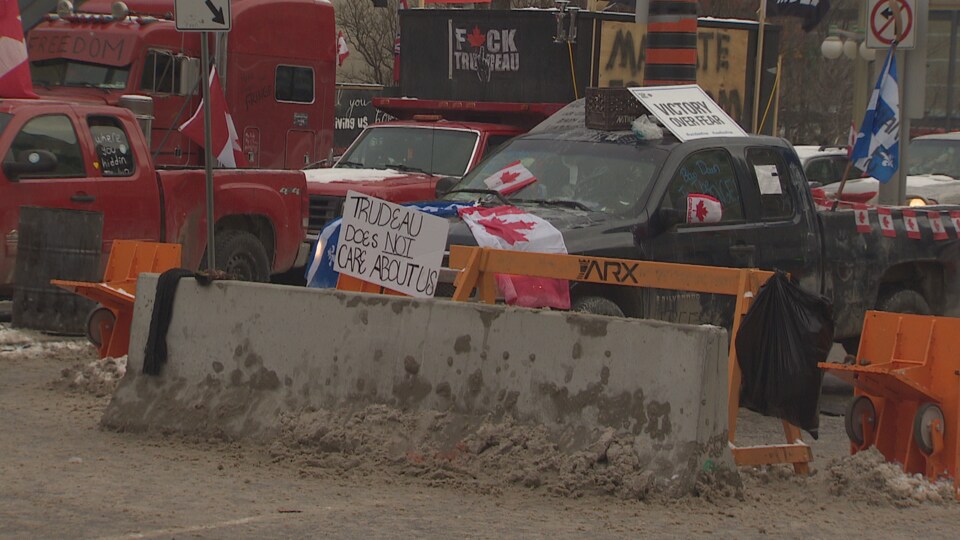 Des camions stationnés derrière des blocs de béton, avec des slogans anti-Trudeau et des drapeaux du Canada et du Québec.