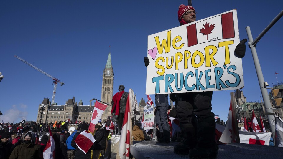 A protester holds a sign reading 'We support truckers' in front of a crowd outside parliament in Ottawa