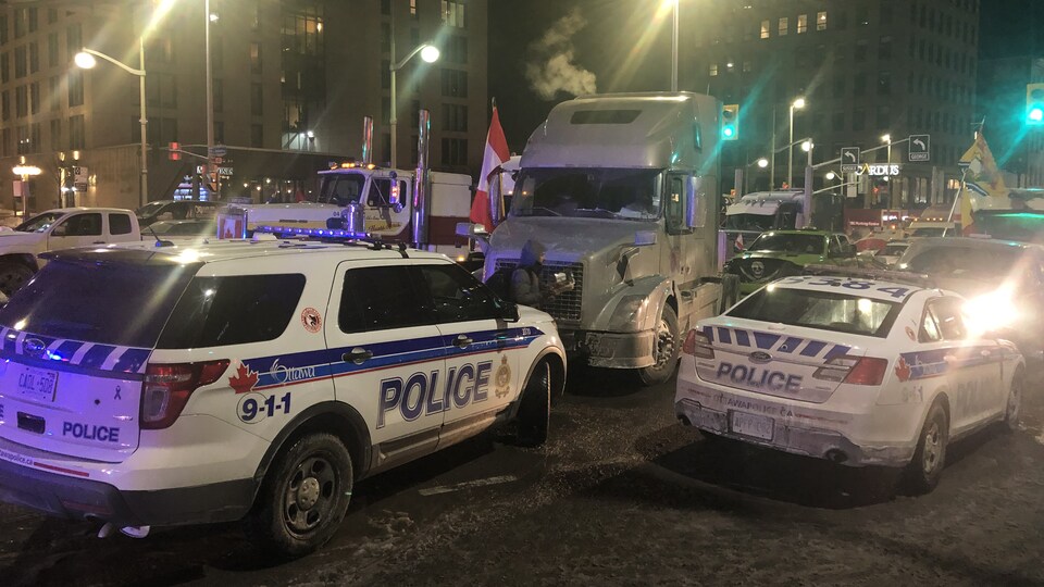 Des voitures de police stationnées devant des camions au milieu de la route.