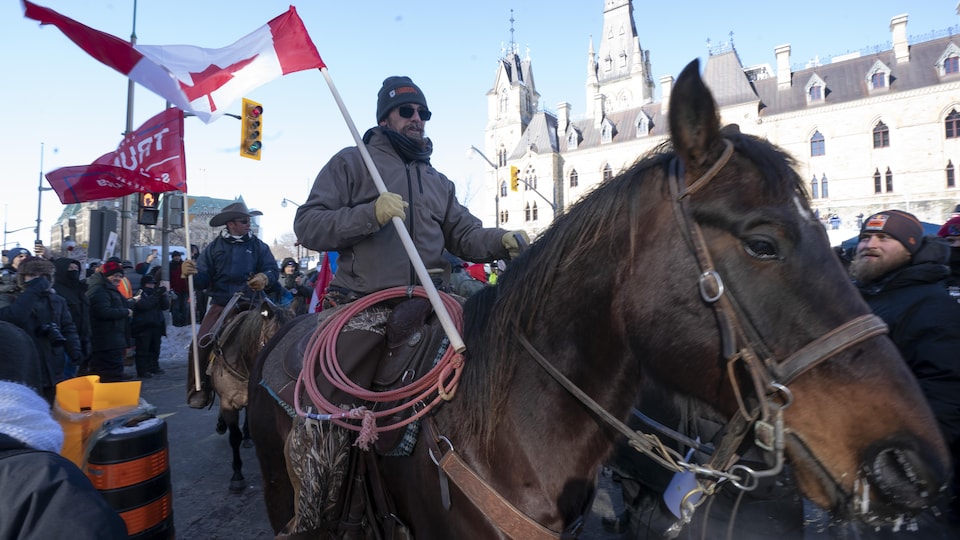 Deux manifestants montent à cheval devant des camions stationnés devant la colline du Parlement lors d'une manifestation contre les restrictions liées à la COVID-19, à Ottawa.
