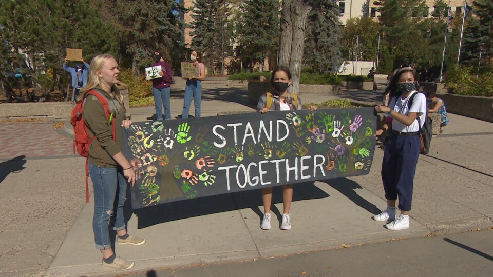 Trois manifestantes tiennent une pancarte où il est inscrit en anglais « stand together ».