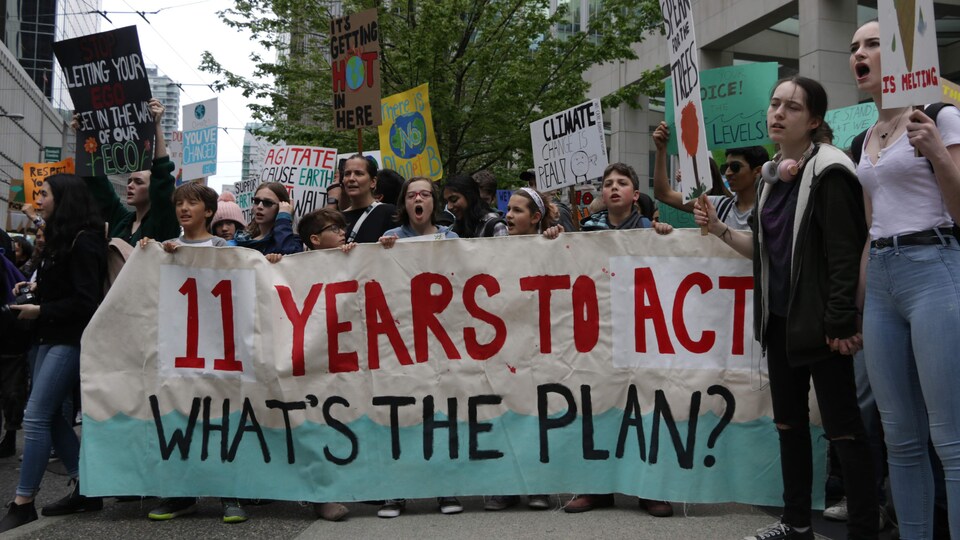 Des jeunes manifestants tiennent une bannière qui lit « 11 ans pour agir, quel est le plan? ».