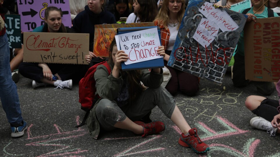Un élève est assis par terre et tient une affiche qui lit « nous devons arrêter les changements climatiques ».