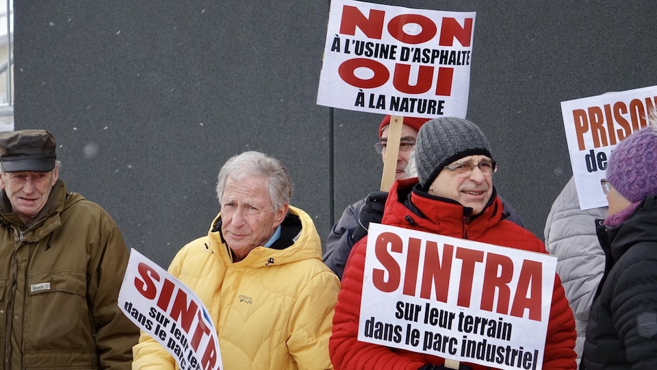 Des manifestants tiennent des pancartes, regroupés devant une tour à bureaux.