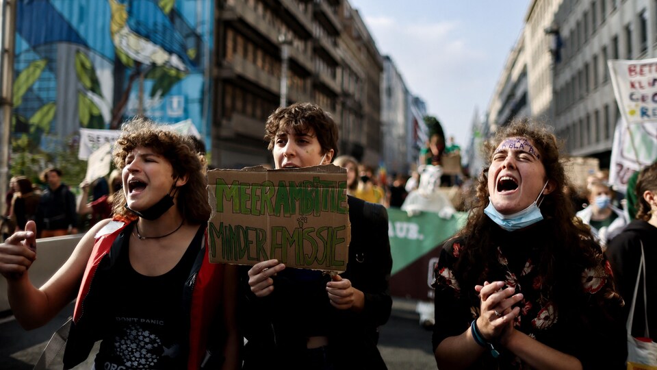 Trois jeunes brandissant une pancarte, avec une foule derrière.