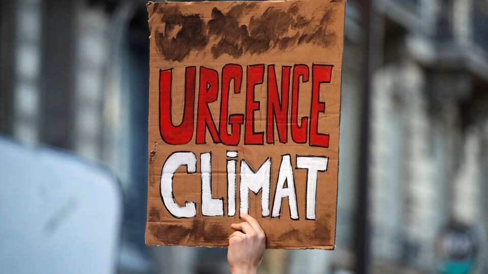 Une personne tient une pancarte sur laquelle on peut lire : « Urgence climat ».