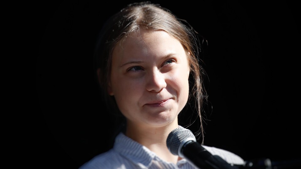 Greta Thunberg, en gros plan, sourit en regardant vers la lumière.