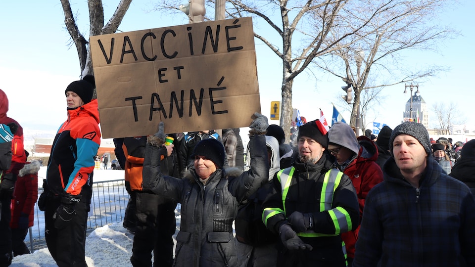 Une femme tient une pancarte sur laquelle on peut lire «Vacciné et tanné».
