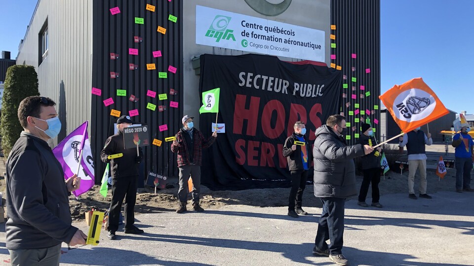 Des syndiqués manifestent avec des drapeaux devant le Centre québécois de formation en aéronautique.