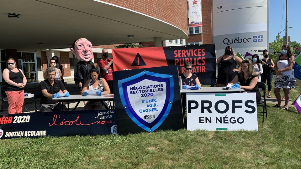 Quatre personnes sont assises à une table à l'extérieur avec des affiches et des pancartes.