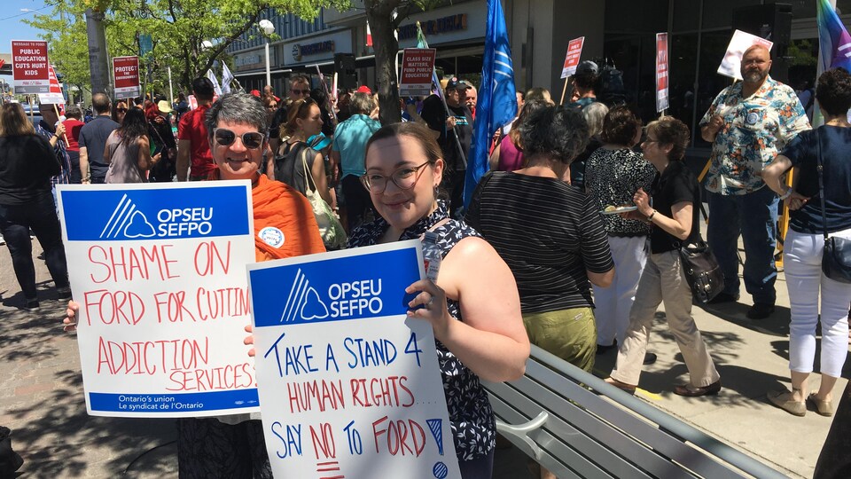 Deux femmes tenant des pancartes dénonçant les politiques de Doug Ford lors d'une manifestation. 
