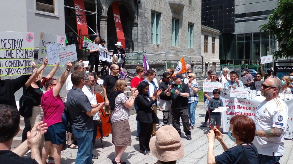 Plusieurs personnes manifestent avec des pancartes devant un établissement au centre-ville de Montréal.
