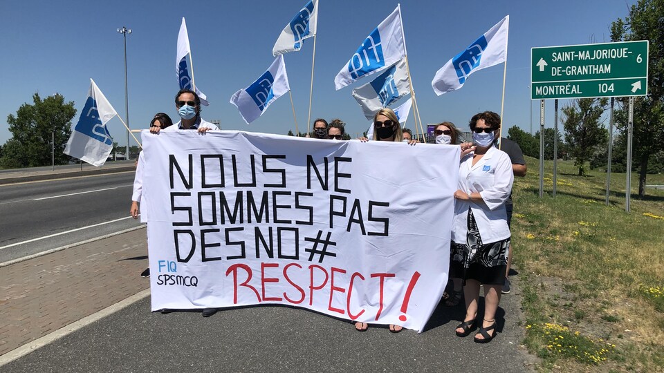 Des professionnels de la santé tiennent une affiche sur laquelle il est écrit «Nous ne sommes pas des numéros».